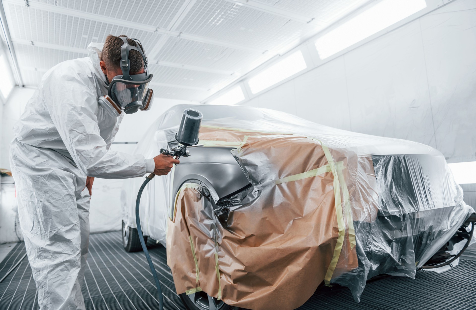 Painting job in progress. Caucasian automobile repairman in uniform works in garage